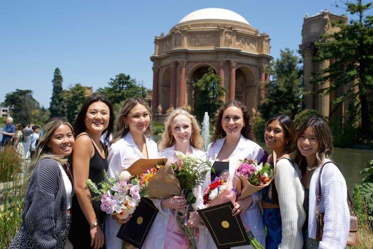 Smiling 学生 wearing white coats in front of the Palace of Fine Arts