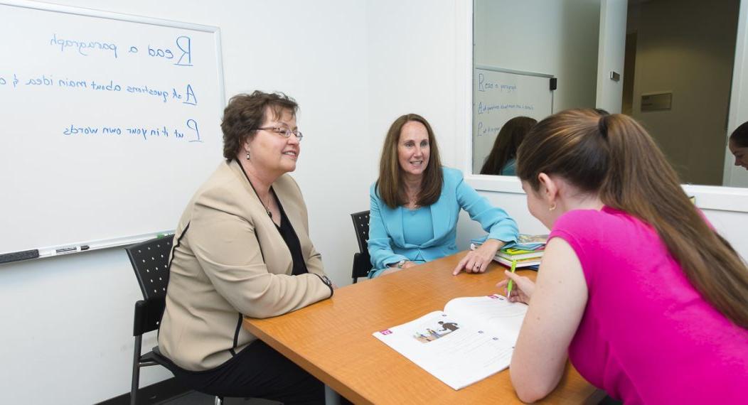 Image shows two Speech-Language Pathology faculty members sitting across a table from a student. 